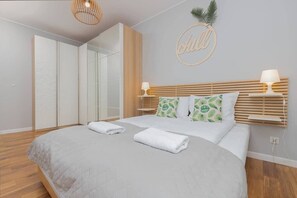 A neatly made bed with white linens and two pillows, a bedside table with a lamp, a wardrobe with sliding doors, and a wall decoration with the word "Chill".