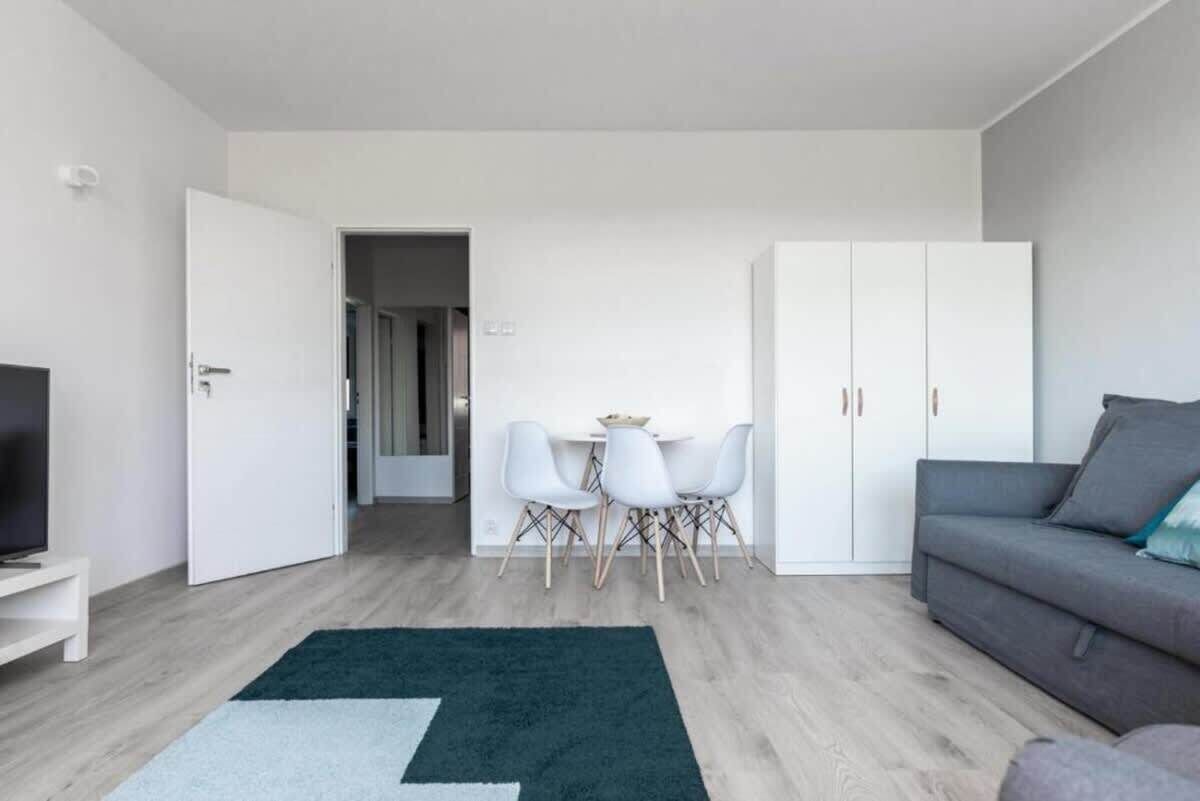 A modern living room with a grey sofa, a TV stand, a dining area with a table and chairs, and a wardrobe.