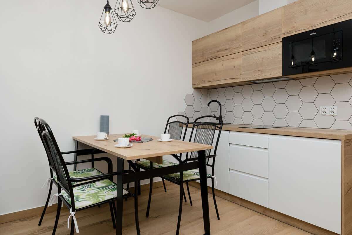 Una cocina moderna con encimera de madera, armarios blancos, microondas negro y salpicadero de azulejos hexagonales.