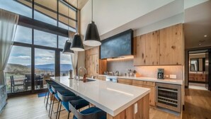 A modern kitchen with a large island, bar stools, and a view of the mountains. - One Snowmass East 703 (Snowmass)