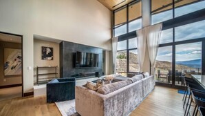 A modern living room with a large TV, comfortable seating, and a view of the outdoors. - One Snowmass East 703 (Snowmass)