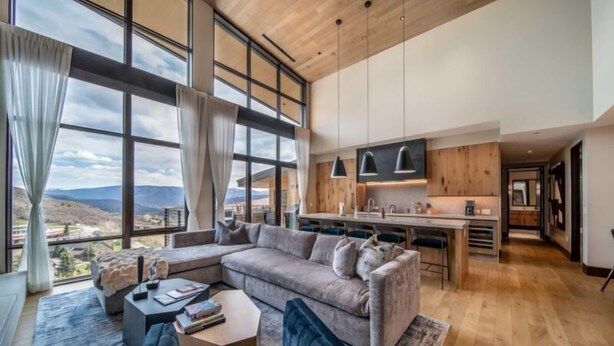 A spacious living area with a large window, a sofa, a coffee table, and a kitchen area with modern appliances. - One Snowmass East 703 (Snowmass)