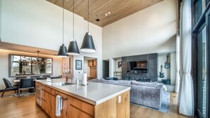 A modern kitchen with wooden cabinets, a large island, pendant lights, and a dining area with chairs. - One Snowmass East 703 (Snowmass)