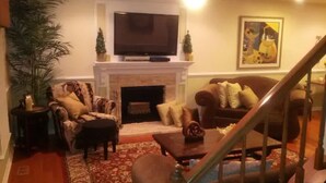 A living room with a fireplace, a television, and a staircase. - Mini Mansion 4,100 sf NCSU/Downtown, 6br, 10 beds (Raleigh)