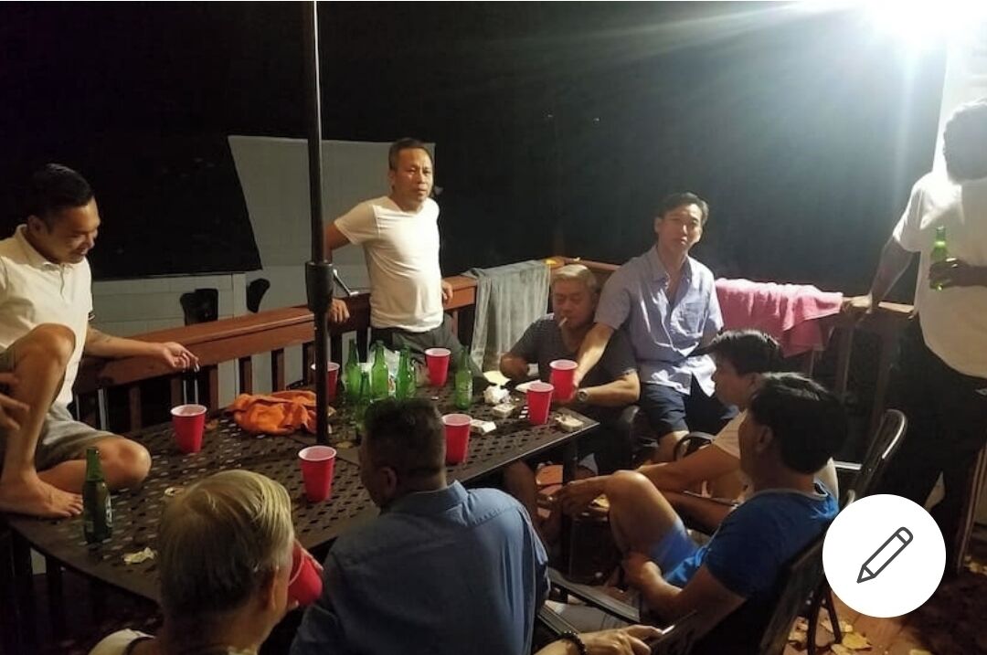 A group of people seated around a table with red cups and bottles, in a dimly lit indoor setting.