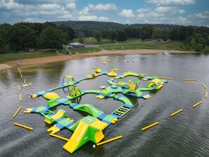 Parque acuático al aire libre con diversas estructuras inflables y una zona de playa de arena.
