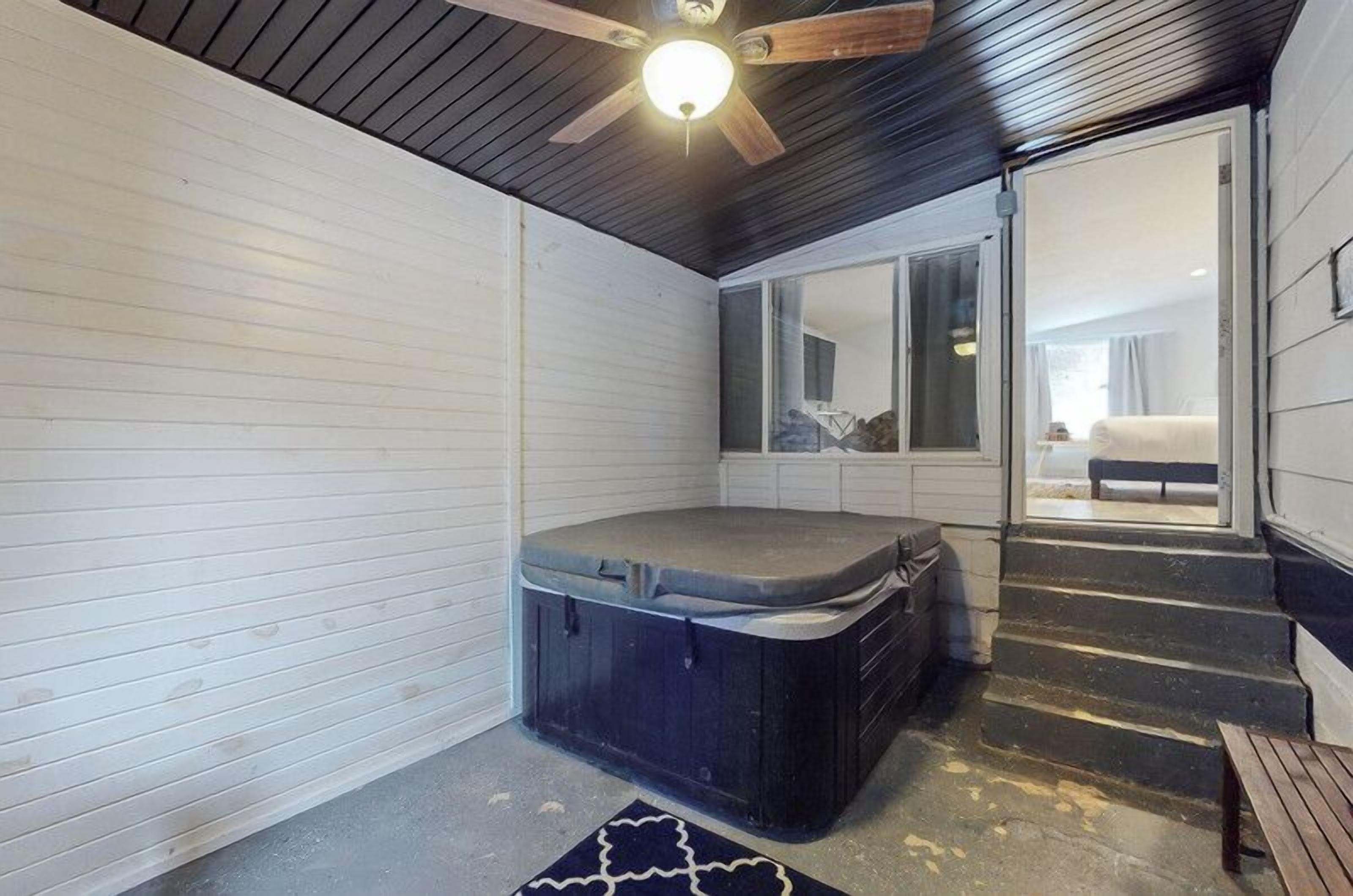 Quarto compacto com hidromassagem, ventilador de teto e vista para um quarto através de uma porta de vidro.