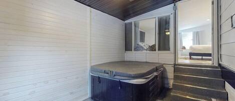 Quarto compacto com hidromassagem, ventilador de teto e vista para um quarto através de uma porta de vidro.