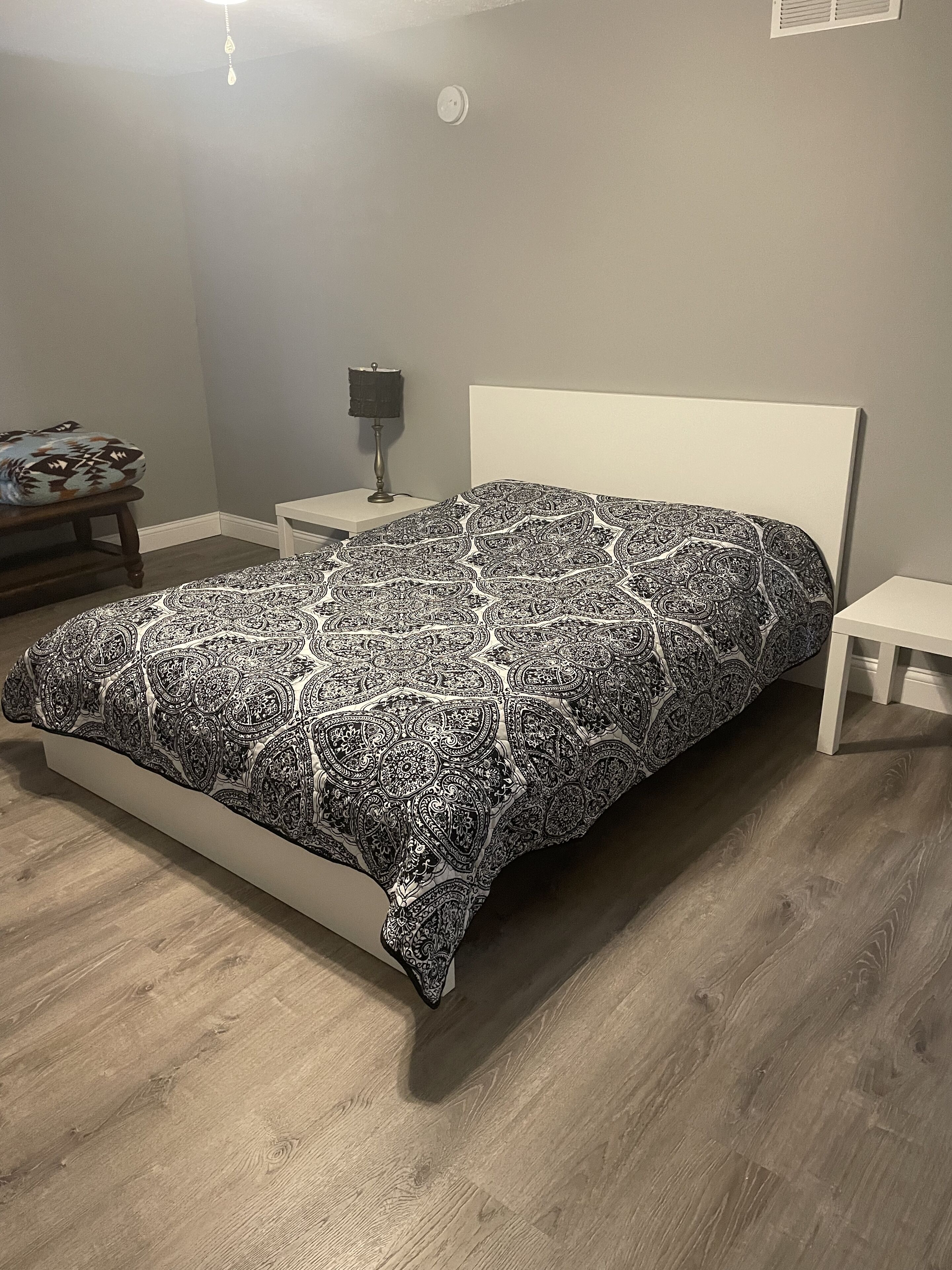 A bedroom with a bed, nightstands, a lamp, and a wall-mounted light fixture.