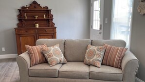 A living room with a beige sofa, patterned cushions, a wooden coffee table, and a vintage wooden cabinet. - Holland Suites, Suite #1 (Williamstown)