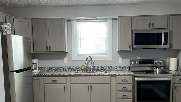 A kitchen with light gray cabinets, a stainless steel refrigerator, a microwave, and an oven. - Holland Suites, Suite #1 (Williamstown)