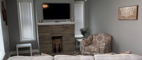 A living room with a grey sofa, a fireplace, a television, and a ceiling fan.