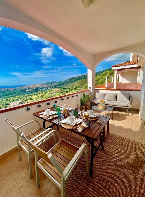 A balcony with a table set for breakfast, overlooking a lush landscape.
