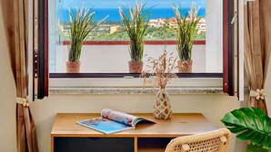Une pièce avec une table en bois, une chaise et une vue sur la mer par une fenêtre ornée de rideaux.