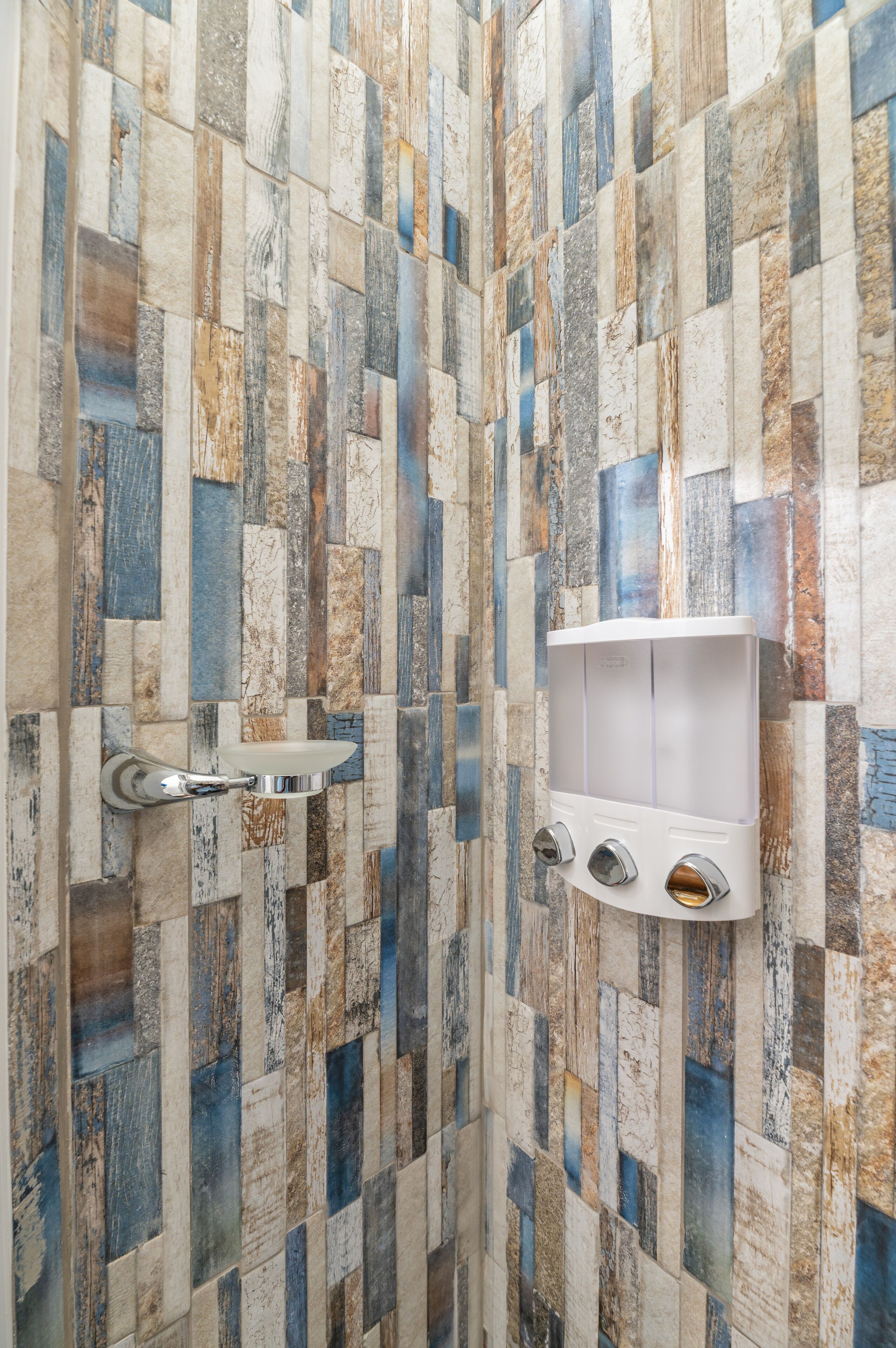 A bathroom with a mosaic tile wall and a white soap dispenser mounted on it.
