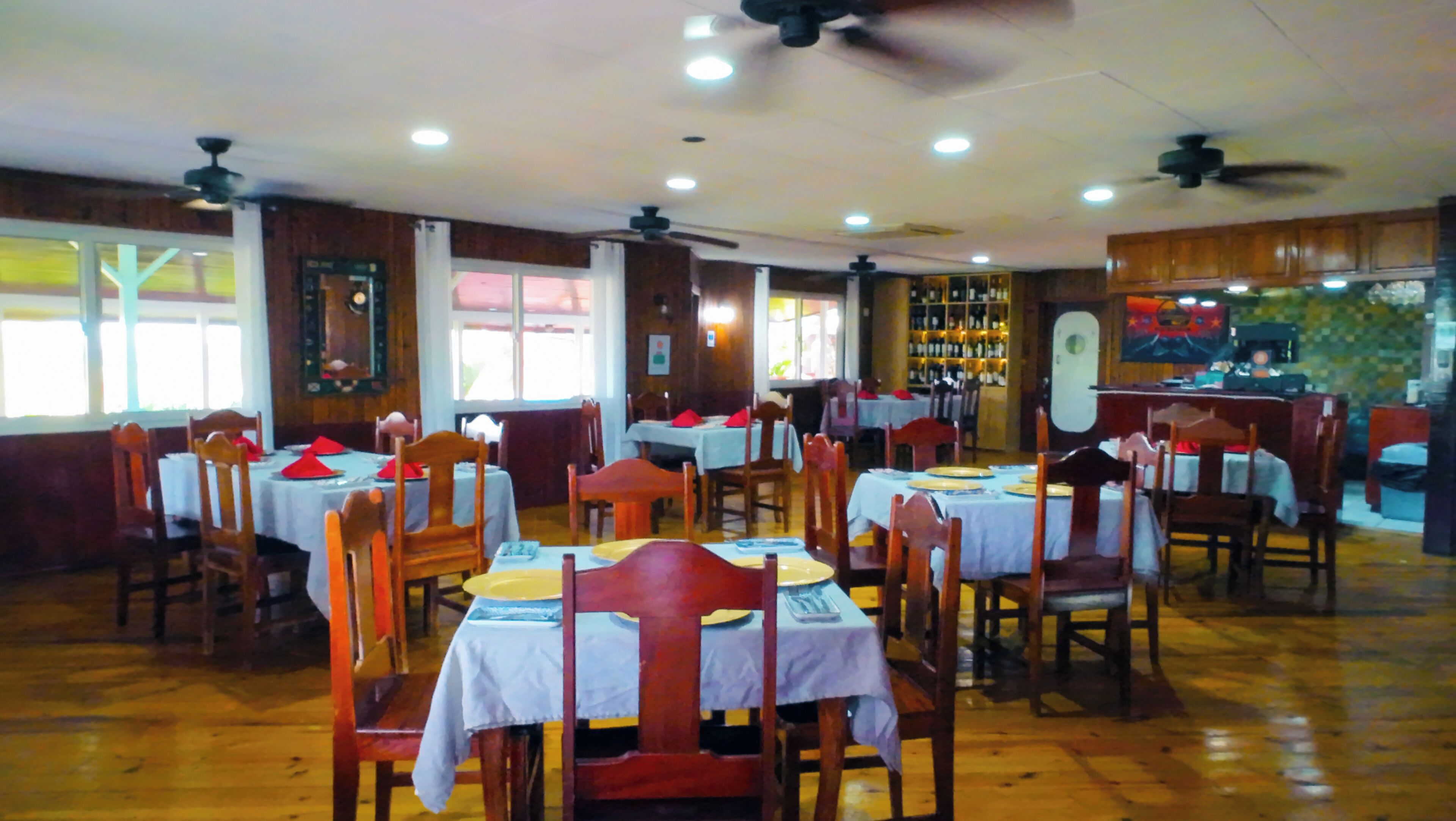 A restaurant with multiple tables and chairs, ceiling fans, and a bar area.