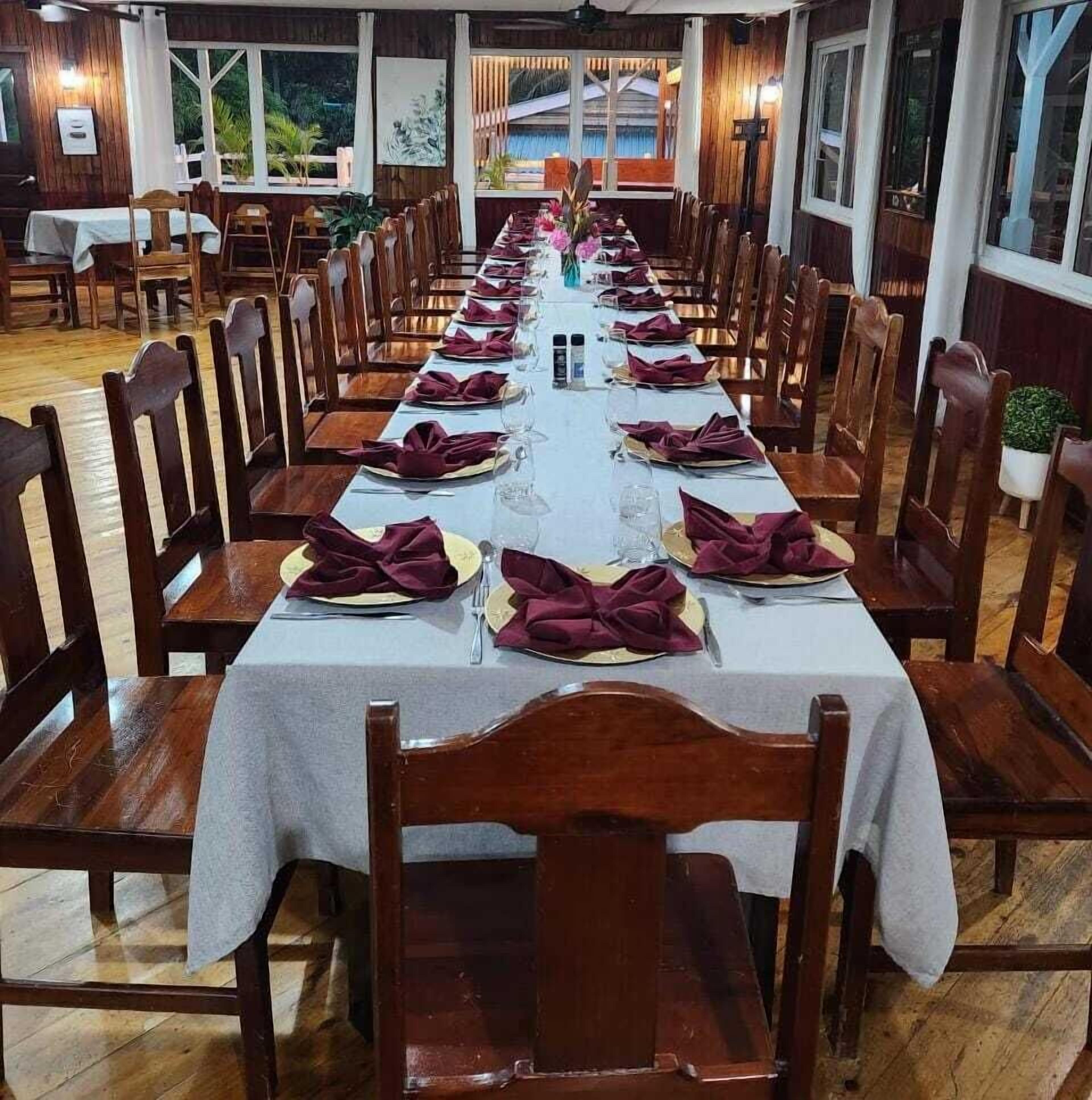 Una larga mesa de comedor dispuesta con sillas, mantel blanco y servilletas moradas.