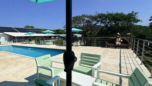 A pool area with green chairs, a table, and umbrellas.
