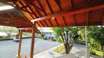 Un espacio al aire libre techado con estructura de madera, un camino pavimentado y un edificio al fondo.