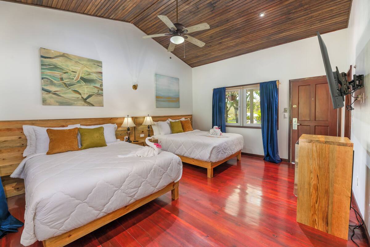 A hotel room with two beds, wooden headboards, a ceiling fan, and a wooden desk.