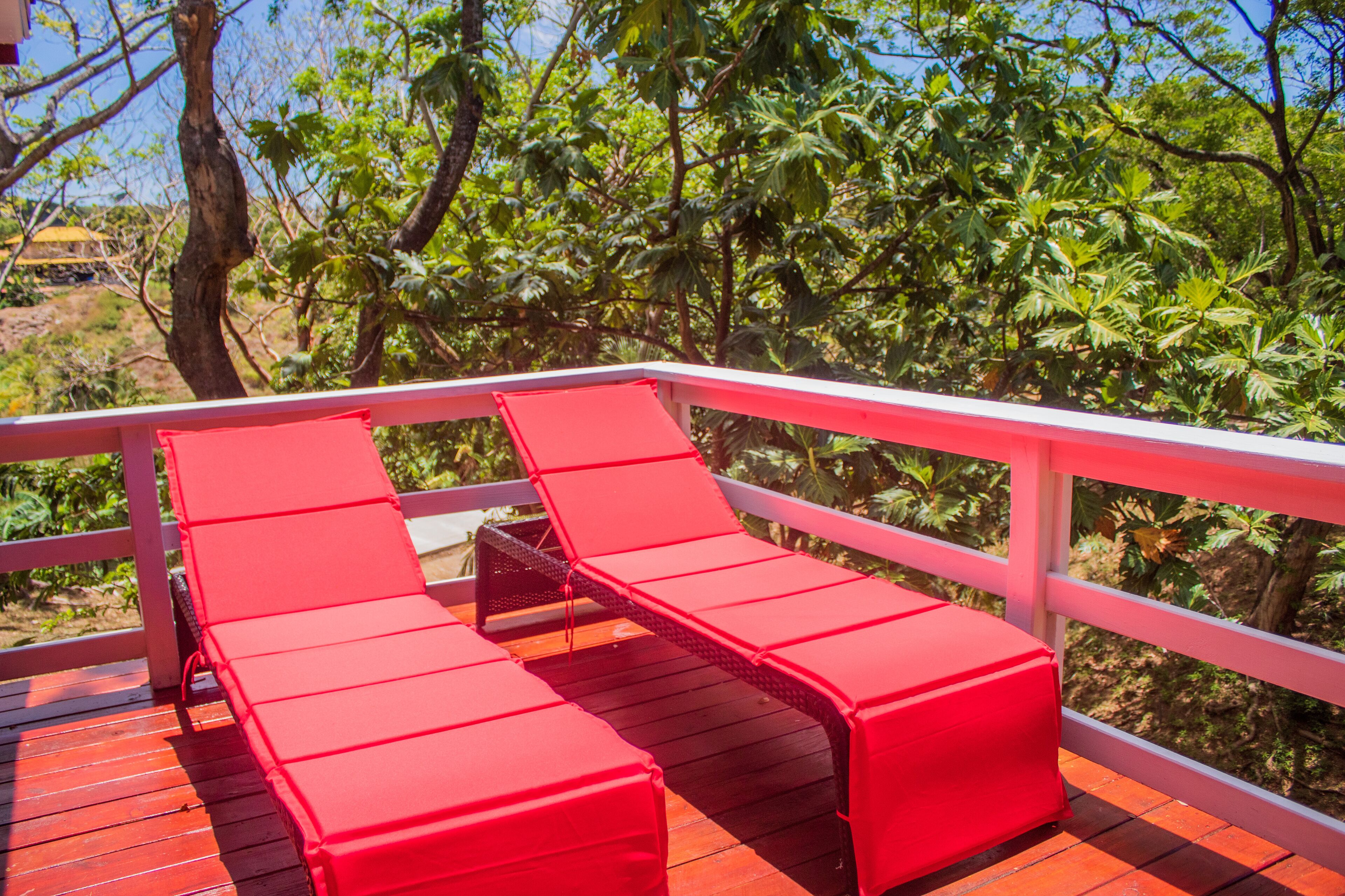 A wooden deck with red lounge chairs and a white railing.