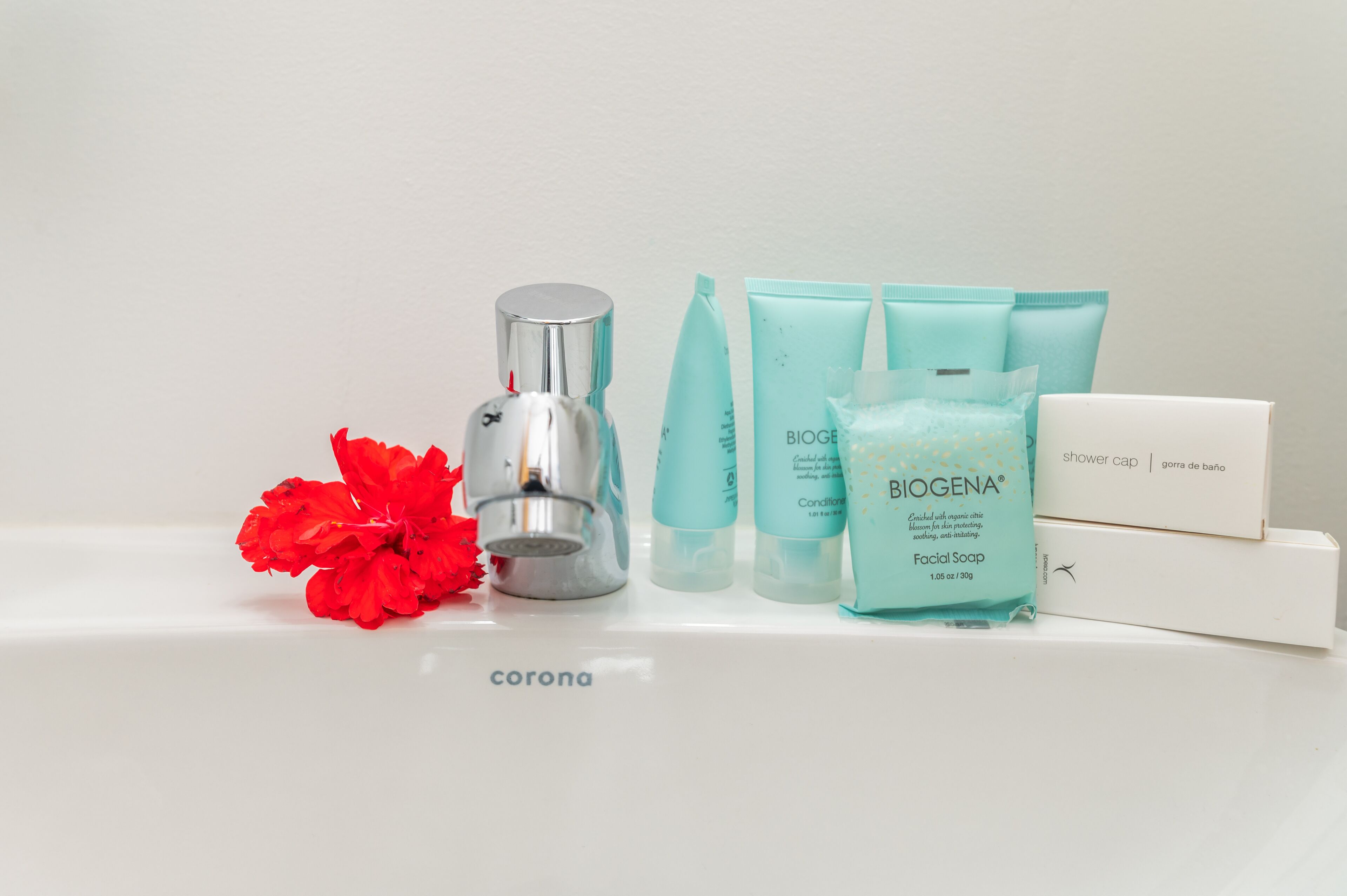 A bathroom counter with various toiletries including a facial soap, shower cap, and a bottle of Biogena facial soap.