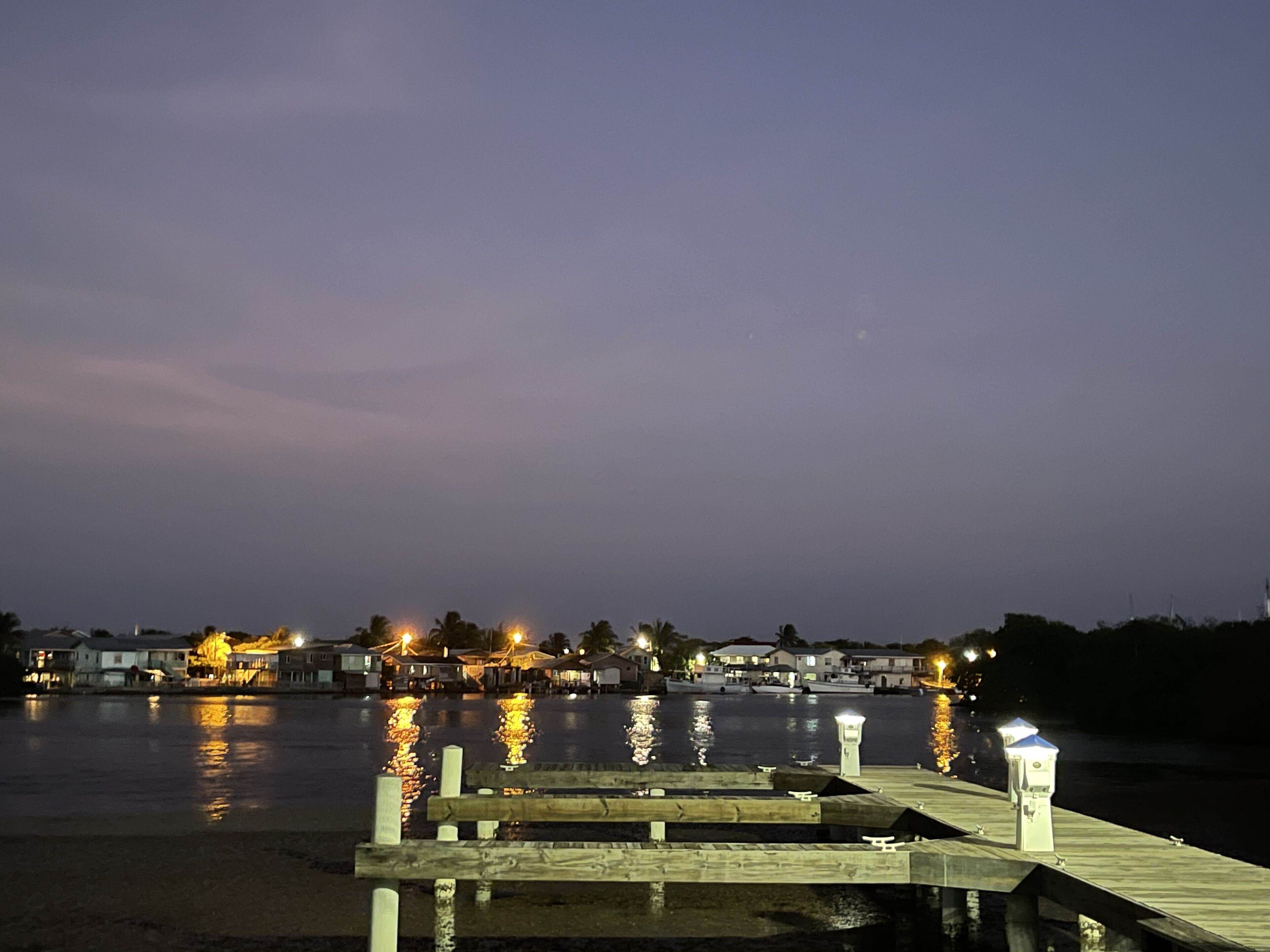 Una propiedad frente al agua con muelle, barcos y edificios iluminados que se reflejan en el agua.