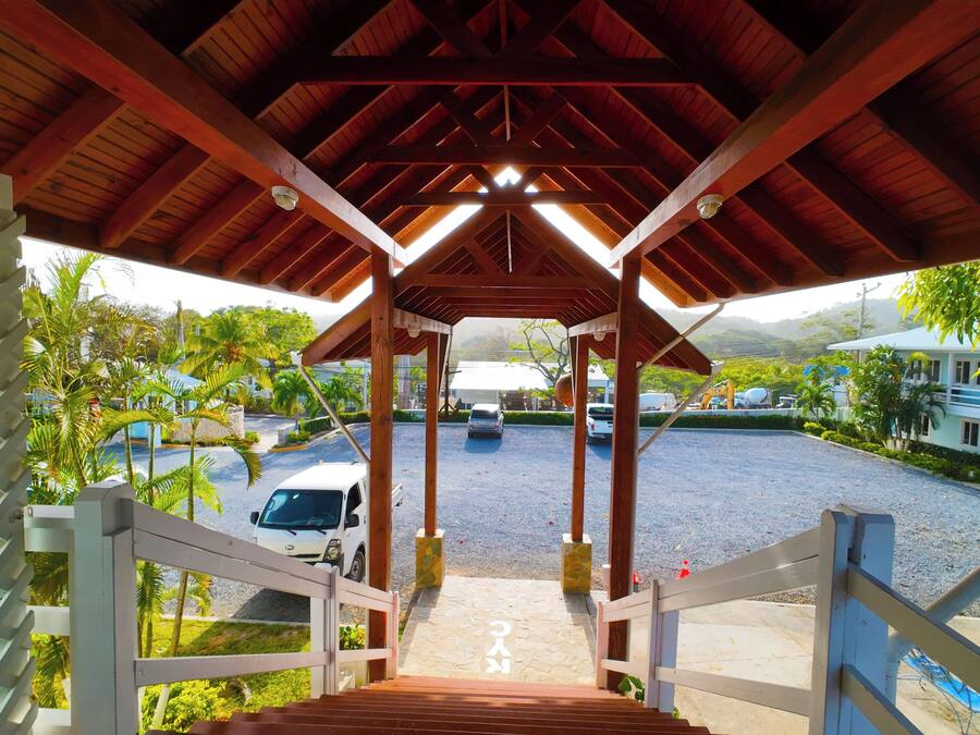 A covered walkway leading to a parking area with a view of a building and palm trees.