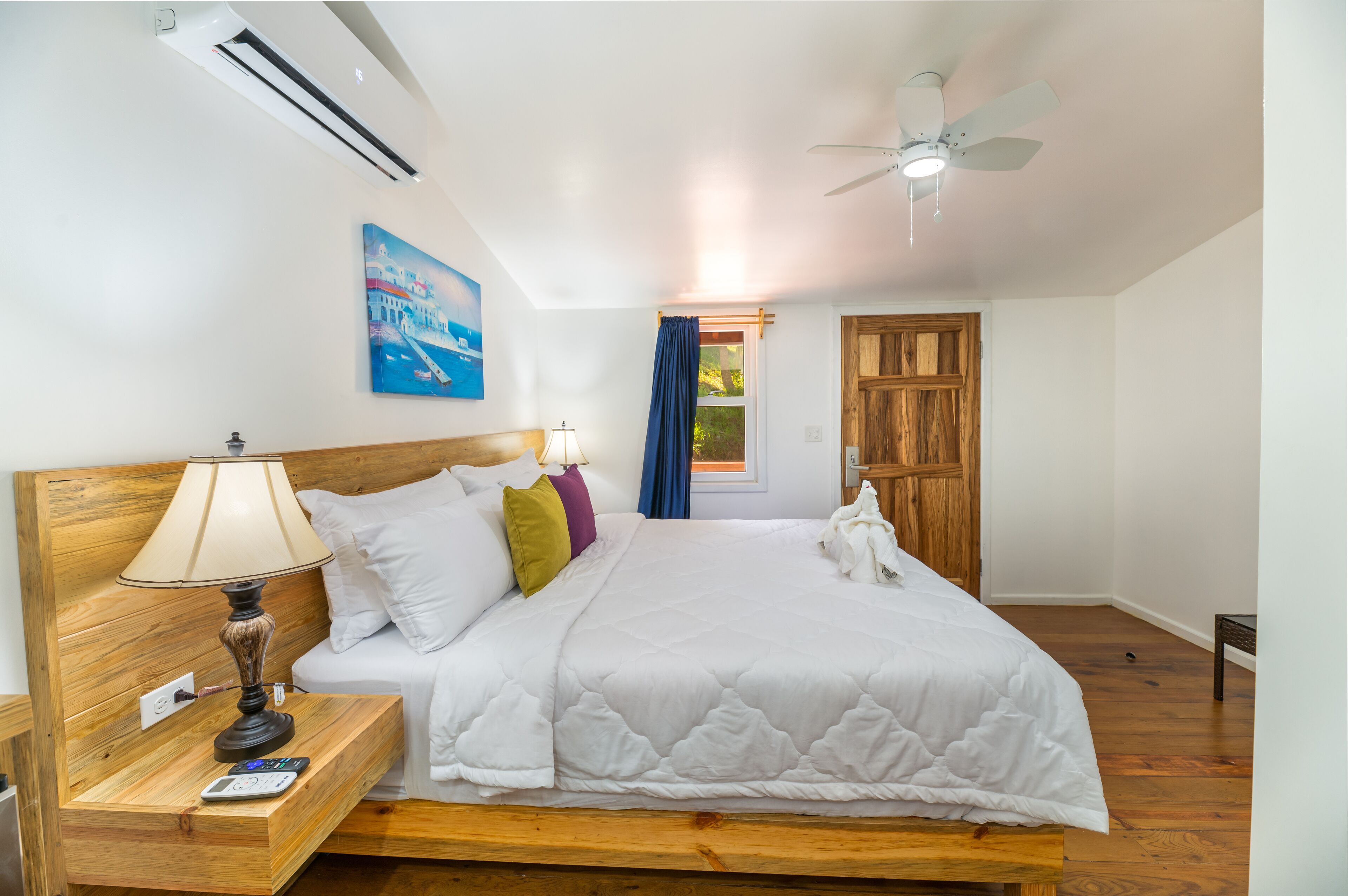 Une chambre à coucher avec une tête de lit en bois, un lit avec une literie blanche, une table de chevet avec une lampe, un climatiseur et un ventilateur de plafond.