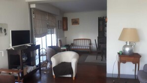 A living room with a sofa, armchair, television, and a lamp on a side table. - Family home with sea view (Royan)