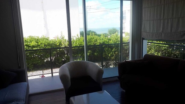 A room with large windows, a white chair, a brown sofa, and a small table. - Family home with sea view (Royan)