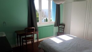 A bedroom with a bed, two wooden chairs, a window with curtains, and a radiator. - Family home with sea view (Royan)