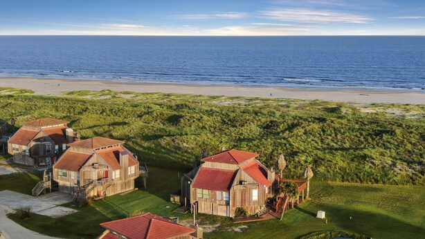 Une propriété située sur la côte, comprenant plusieurs maisons en bois avec des toits rouges, et bâtie sur une colline verdoyante d’où l’on a vue sur une plage et l’océan.