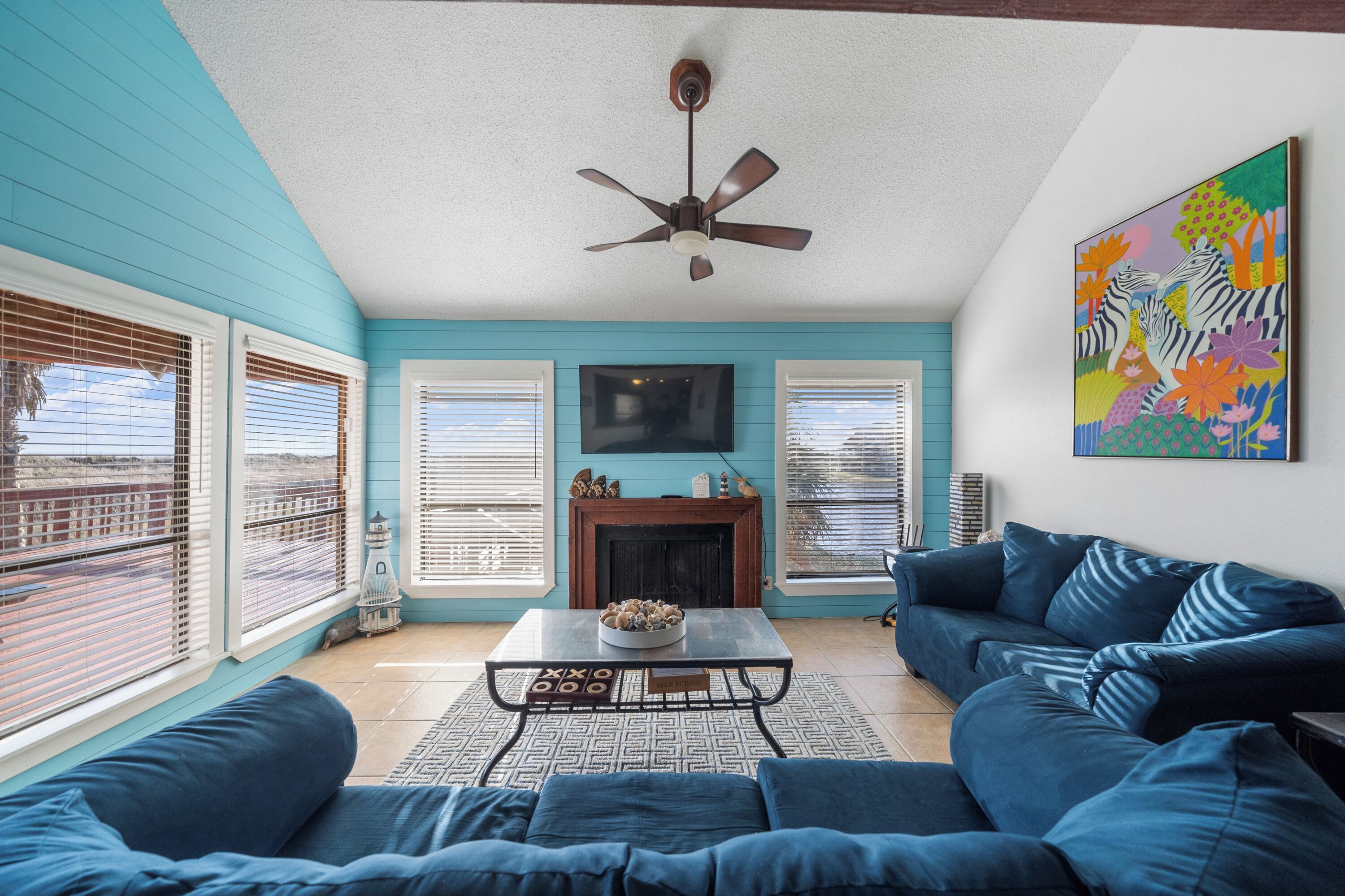 A living room with a blue couch, a coffee table, a fireplace, and a ceiling fan.