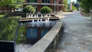 Un patio con un estanque rectangular, un sendero de piedra y un edificio de ladrillo con ventanas grandes.
