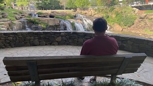 Un hombre sentado en un banco mirando un cascada.