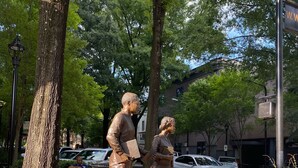 Una estatua de un hombre y una mujer en un parque, con estructuras de ladrillo y árboles.