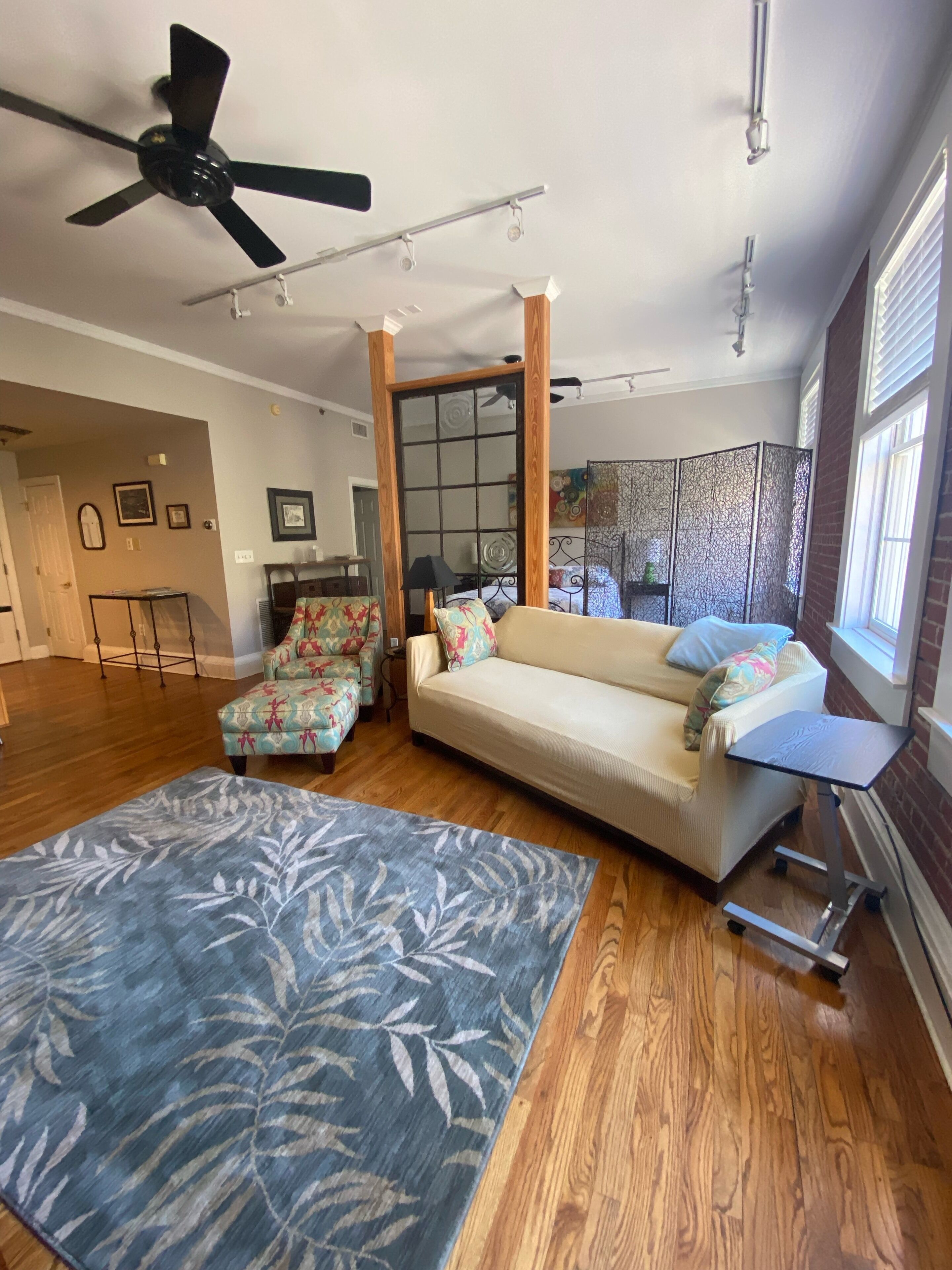 A spacious living room with a sofa, a patterned rug, a ceiling fan, and a sliding glass door leading to another room.
