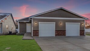 Een garage voor twee auto's, vastgebouwd aan een gelijkvloers huis met een fundering van baksteen en een schuin dak.