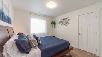 A bedroom with a bed, a window with curtains, a door, and a wall-mounted plant.