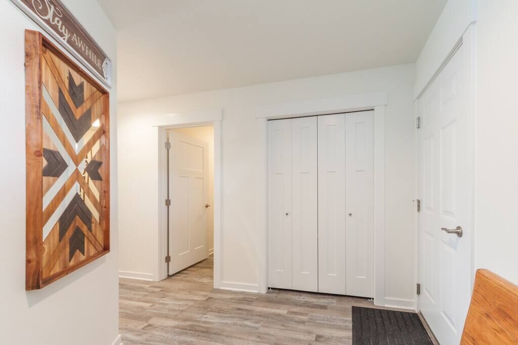 A hallway with a wooden wall art piece, a white door, and a white closet with multiple doors.