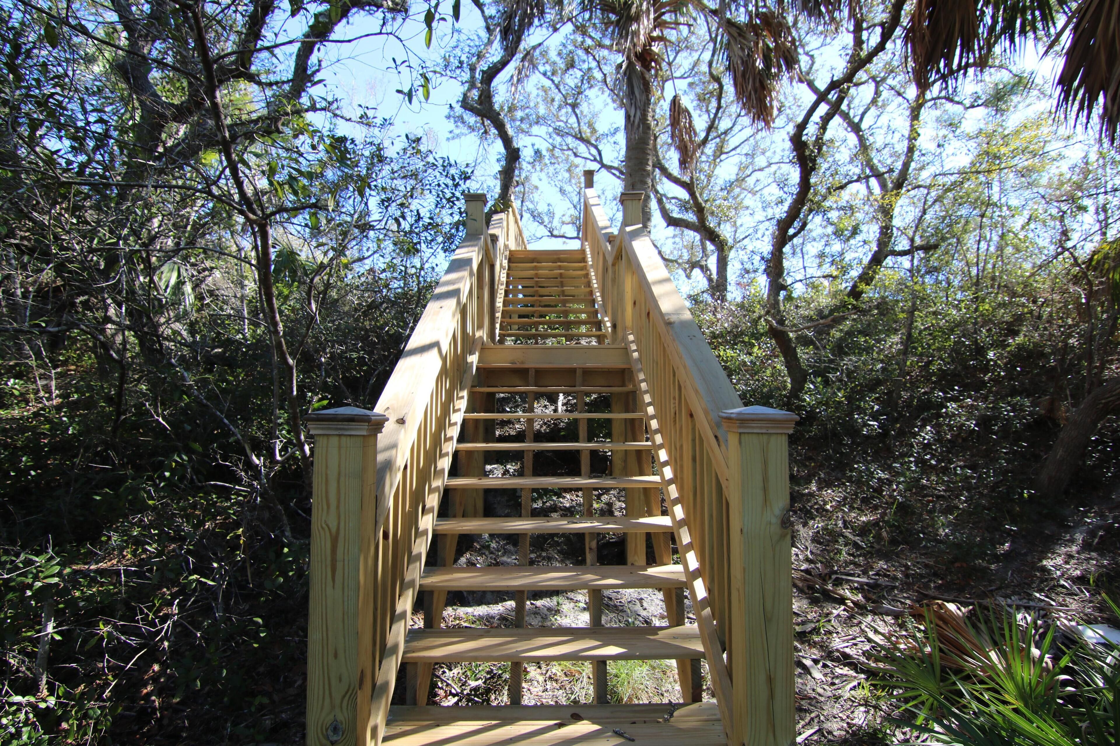 Una escalera de madera que sube hacia un puente en un área boscosa.