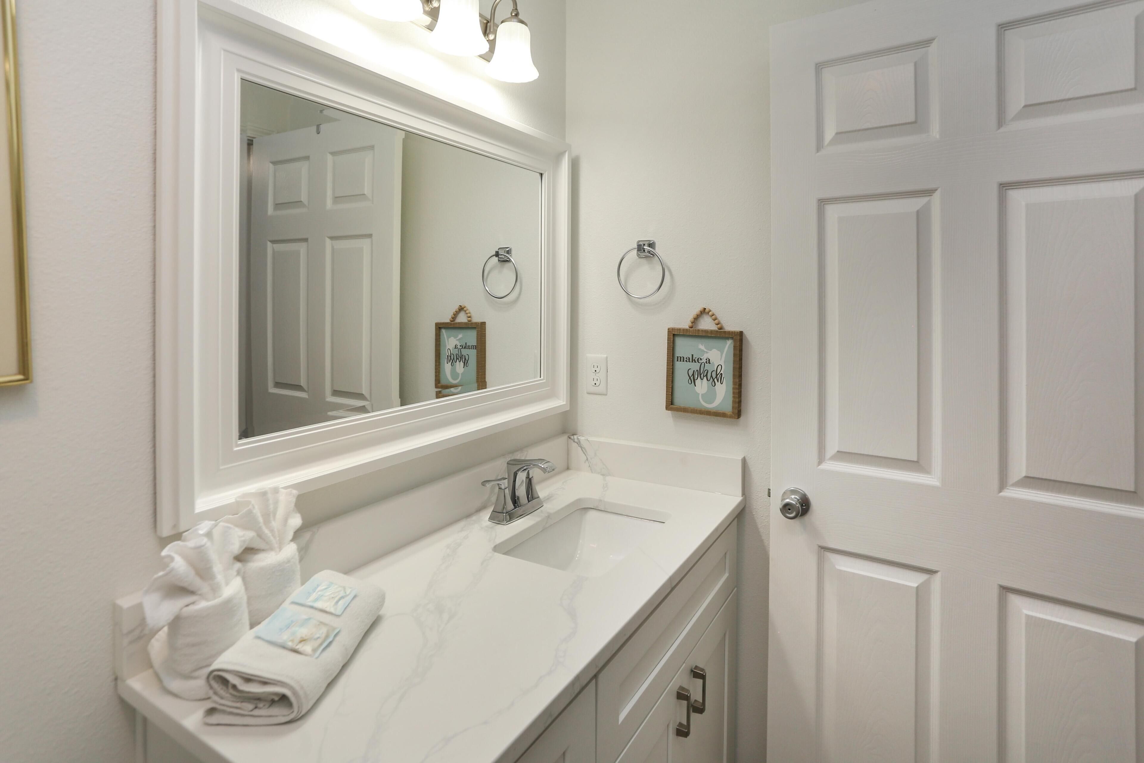 A bathroom with a white vanity, a large mirror, a sink, and a door with a circular handle.
