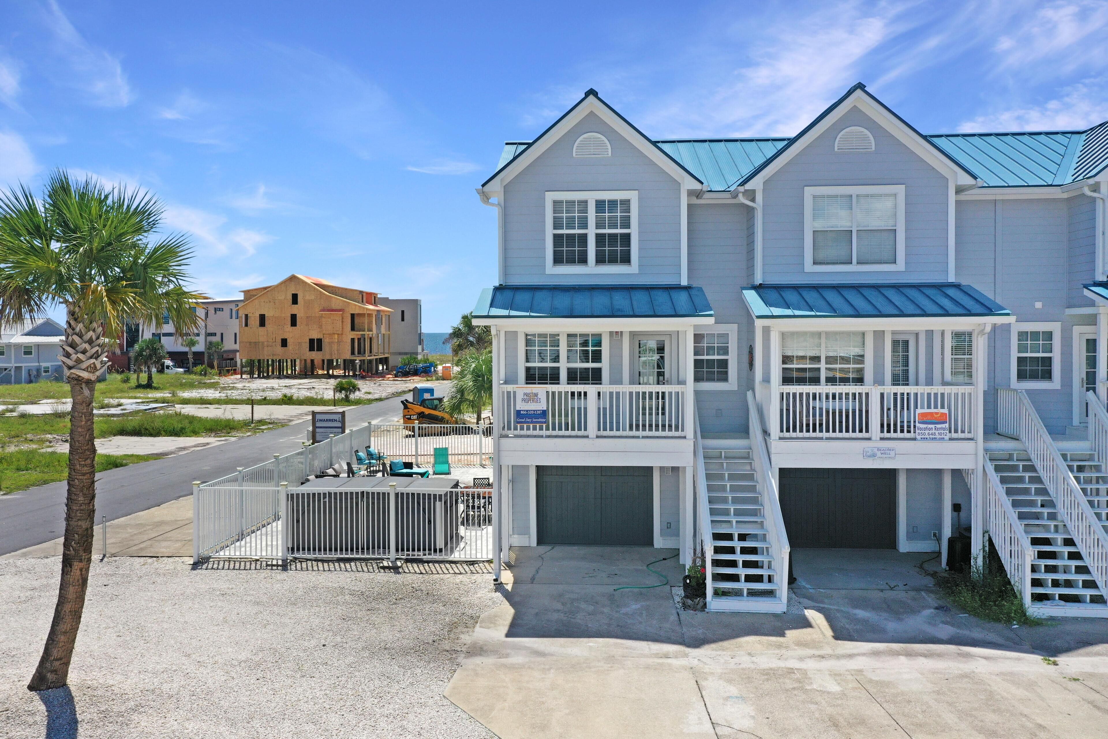 Een twee verdiepingen tellend huis aan het strand, met een overdekte veranda, een garage en een trap naar de bovenverdieping.