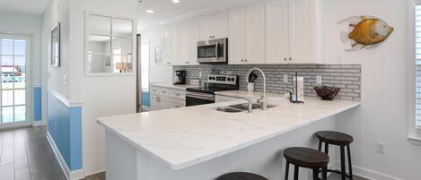 A modern kitchen with white cabinets, a large island with stools, a microwave, and a fish wall decoration.
