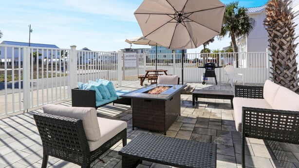 An outdoor patio with wicker furniture, a fire pit, and umbrellas.