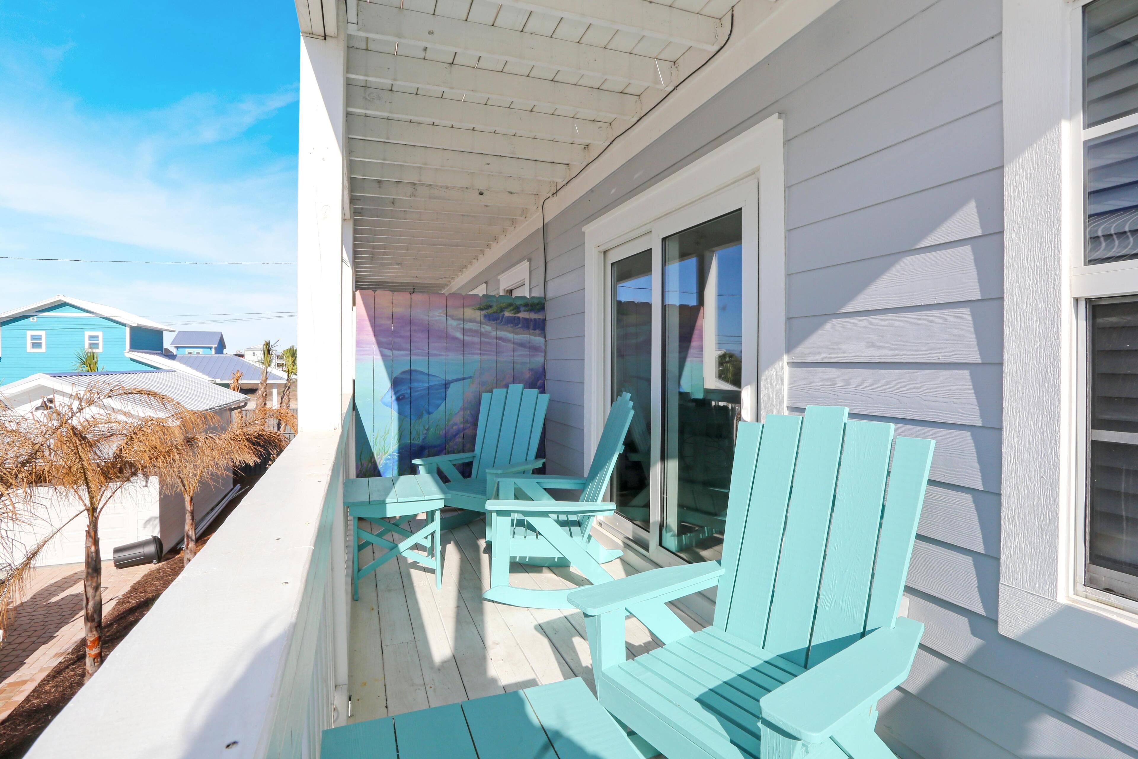 A covered porch with turquoise Adirondack chairs and a glass door leading to a covered area.