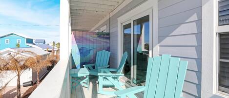 A covered porch with turquoise Adirondack chairs and a glass door leading to a covered area.
