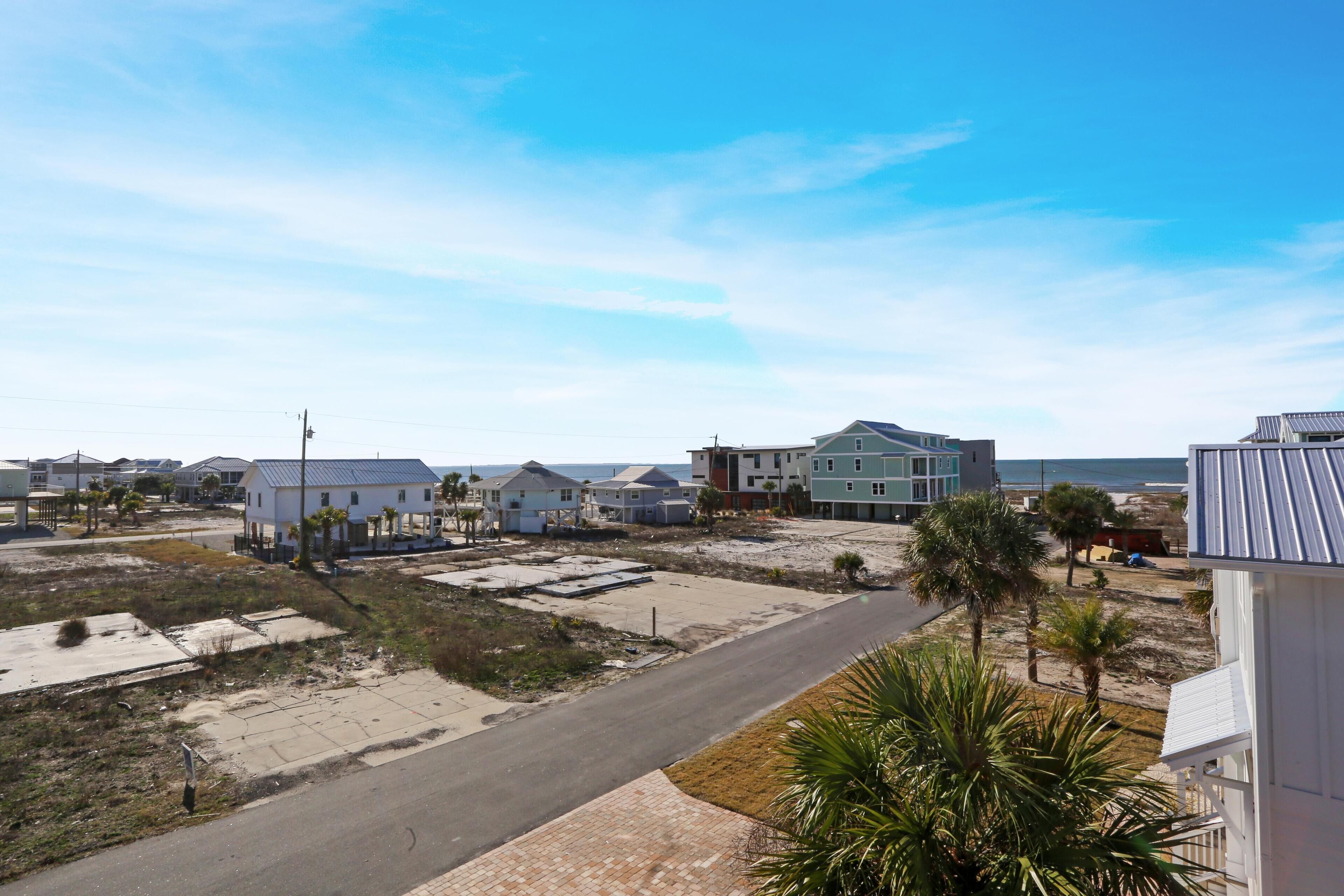 A coastal residential area with houses, a paved road, and a beach in the background.