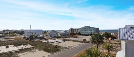 A coastal residential area with houses, a paved road, and a beach in the background.